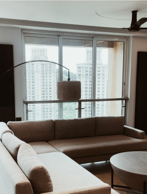 Modern living room interior design with sectional sofa, large windows and city view in Mumbai apartment